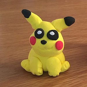 L'image montre une figurine en pâte à modeler représentant un personnage de dessin animé. Ce personnage est de couleur jaune, avec de grandes oreilles pointues. Il a des joues rouges et des yeux noirs avec des pupilles blanches. La posture est assise, et le personnage a un air mignon et stylisé. Les détails tels que les oreilles noires aux extrémités ajoutent une touche de charme à la création.
