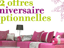 L'image présente un salon avec un canapé moderne et coloré. Le canapé est principalement en rose avec des coussins décoratifs aux motifs variés. Il y a également des touches de gris et de blanc, ajoutant une élégance à l'ensemble. L'arrière-plan est simple, ce qui met en valeur le mobilier. En haut de l'image, le texte indique "2 offres anniversaire optionnelles" en utilisant des couleurs vives, ce qui semble promouvoir une promotion spéciale.