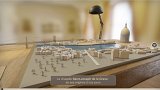 L'image montre une maquette en 3D d'une ville, mettant en évidence la chapelle Saint-Joseph de la Grave. Sur la maquette, on aperçoit des bâtiments représentés en relief et différents éléments du paysage urbain, tels que des arbres. En arrière-plan, on voit un lampadaire qui éclaire la scène, ainsi qu'un dôme, probablement d'un édifice religieux ou public. La maquette semble être présentée sur une surface en bois, donnant une ambiance chaleureuse à l'ensemble. Un texte en bas mentionne le titre de l'image, soulignant l'évolution de la chapelle depuis ses origines jusqu'à nos jours.
