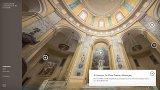 L'image montre l'intérieur d'un bâtiment avec une architecture impressionnante, probablement une église ou un monument historique. On peut voir de hauts murs ornés de colonnes, des décorations murales et une coupole au-dessus, qui laisse entrevoir une belle lumière naturelle. À l'arrière-plan, il y a des œuvres d'art accrochées aux murs. La description mentionne également une cour, la Cour Sainte-Monique, qui est bordée de galeries et accessible par des portiques ouverts. L'atmosphère est à la fois majestueuse et apaisante.
