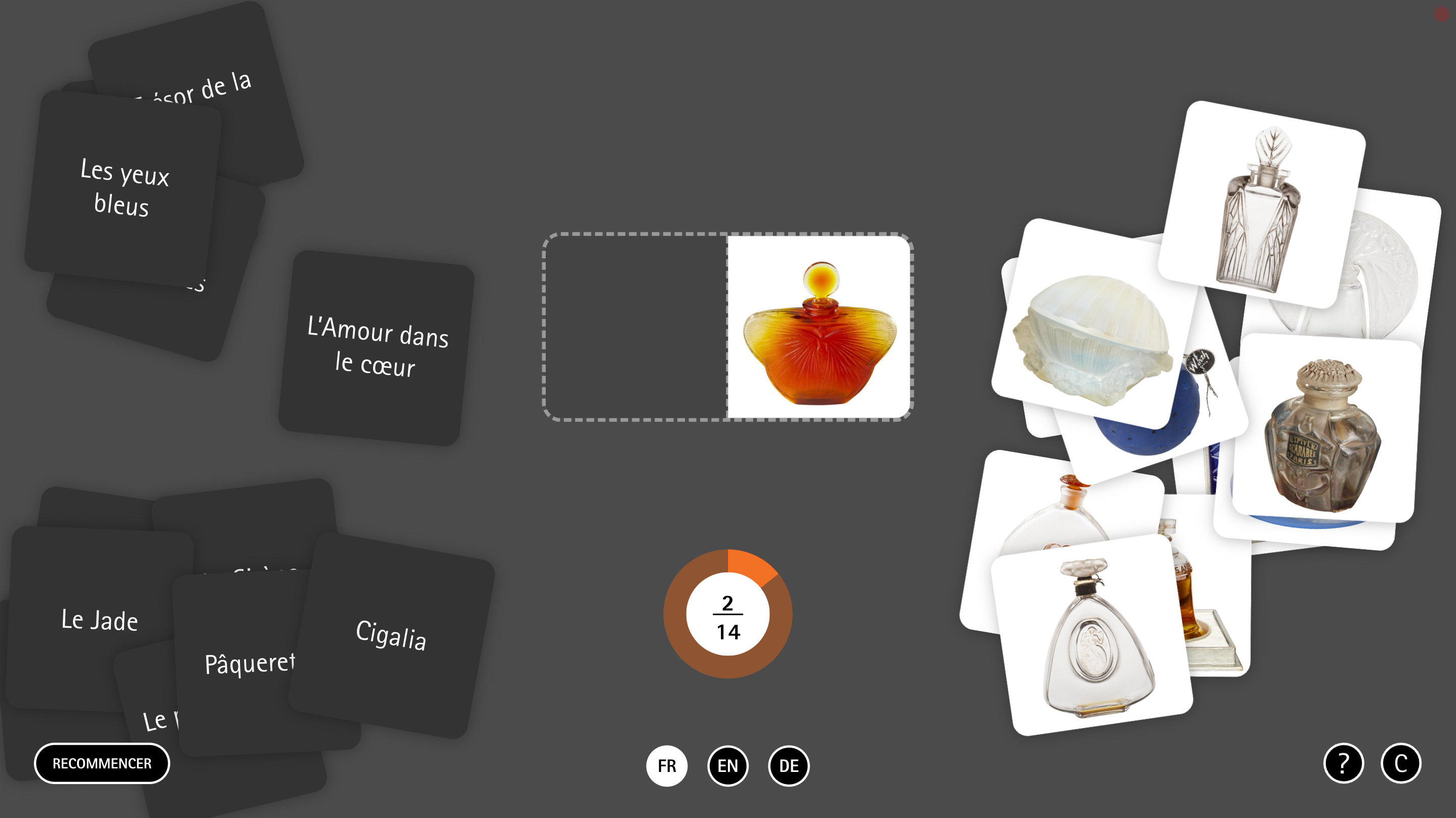 L'image semble illustrer un jeu ou une activité de type carte, avec des cartes noires à gauche contenant des phrases ou des mots, et des cartes blanches à droite présentant des images de flacons ou de bouteilles. Au centre, il y a une image d'un flacon de parfum de couleur orange avec un design élégant. En bas, il y a une indication de progression (2 sur 14) et des options de langue (FR, EN, DE).