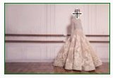 L'image montre une robe élégante en tissu orné, probablement une robe de soirée ou une robe de mariée. La robe a une silhouette ample et raffinée, avec des détails floraux ou des motifs délicats. Elle est présentée contre un fond sobre, ce qui met en valeur sa beauté et son design. L'environnement est lumineux et moderne, ajoutant à l'élégance de la tenue.