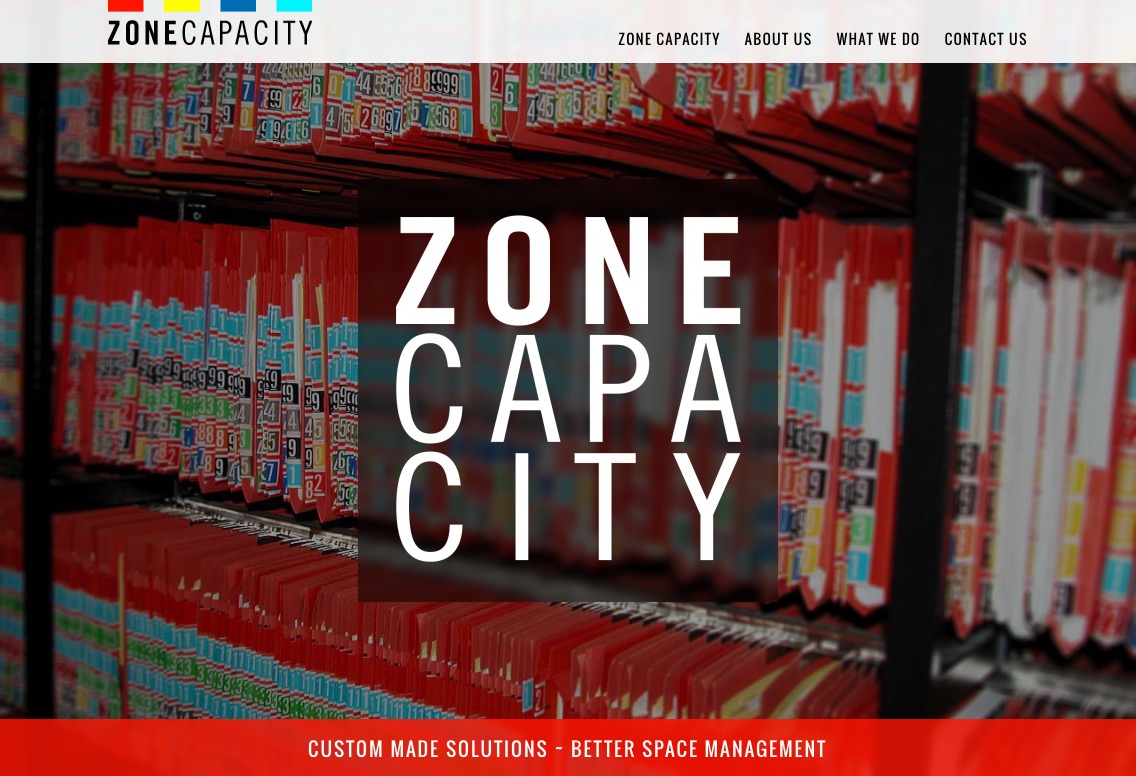 L'image présente un site web intitulé "ZONE CAPACITY". En arrière-plan, on peut voir des rangées de fichiers ou de dossiers organisés sur des étagères, principalement en rouge. Au centre, le nom "ZONE CAPACITY" est affiché en lettres blanches et larges, mettant en avant l'identité de l'entreprise. Le site semble se concentrer sur des solutions sur mesure pour une meilleure gestion de l'espace, comme indiqué par le texte supplémentaire en bas de la page.
