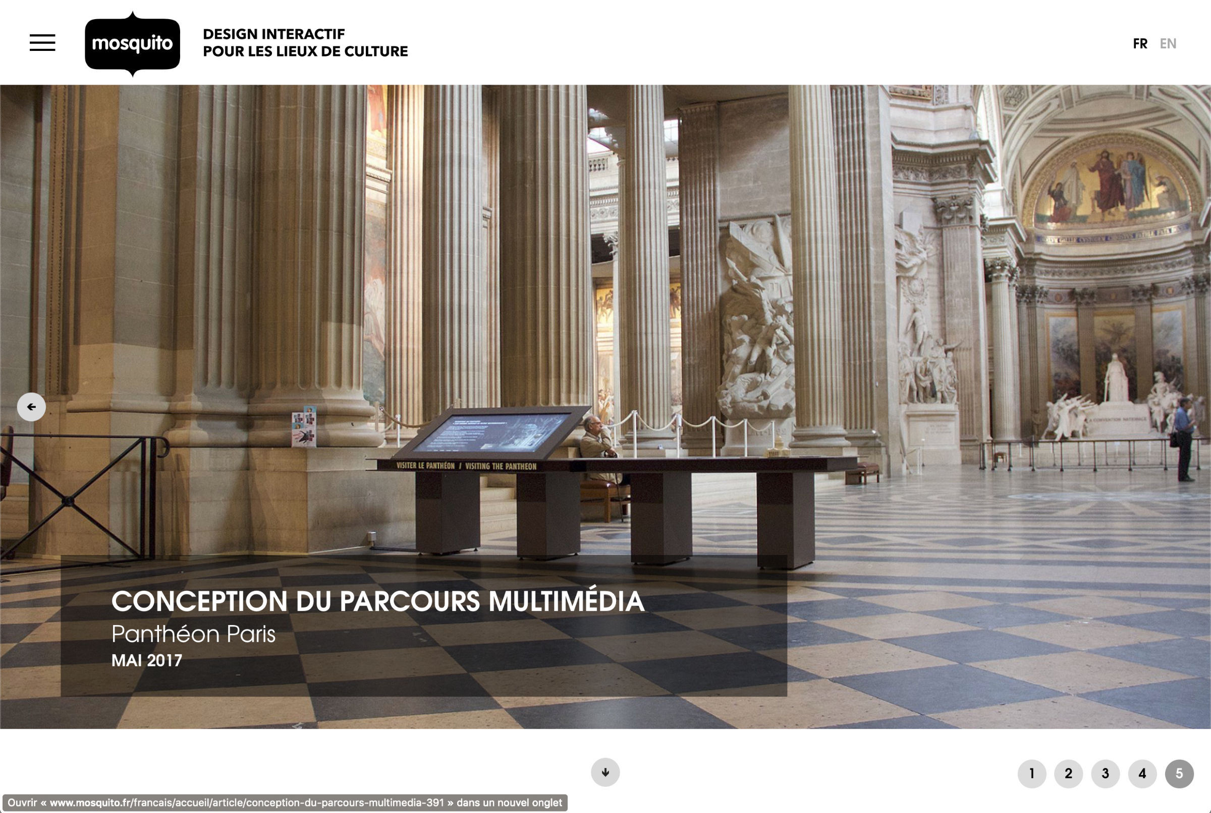 L'image montre l'intérieur d'un grand espace architectural, probablement un musée ou un monument historique, avec des colonnes majestueuses et un plafond élevé. Au centre, il y a une table ou un écran interactif, qui semble être destiné à offrir des informations multimédias aux visiteurs. L'éclairage est naturel, provenant des fenêtres situées en hauteur. L'atmosphère générale semble à la fois élégante et accueillante, invitant à l'exploration.