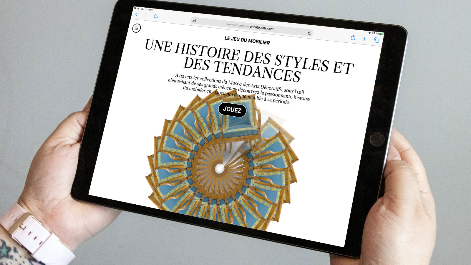 L'image montre une personne tenant une tablette dans ses mains. À l'écran, on peut lire "UNE HISTOIRE DES STYLES ET DES TENDANCES" avec des éléments graphiques colorés en forme de spirale. Il y a aussi un bouton "Jouez" en bas de l'écran, suggérant une interaction ou un jeu lié à l'histoire du mobilier. La présentation semble être moderne et engageante.