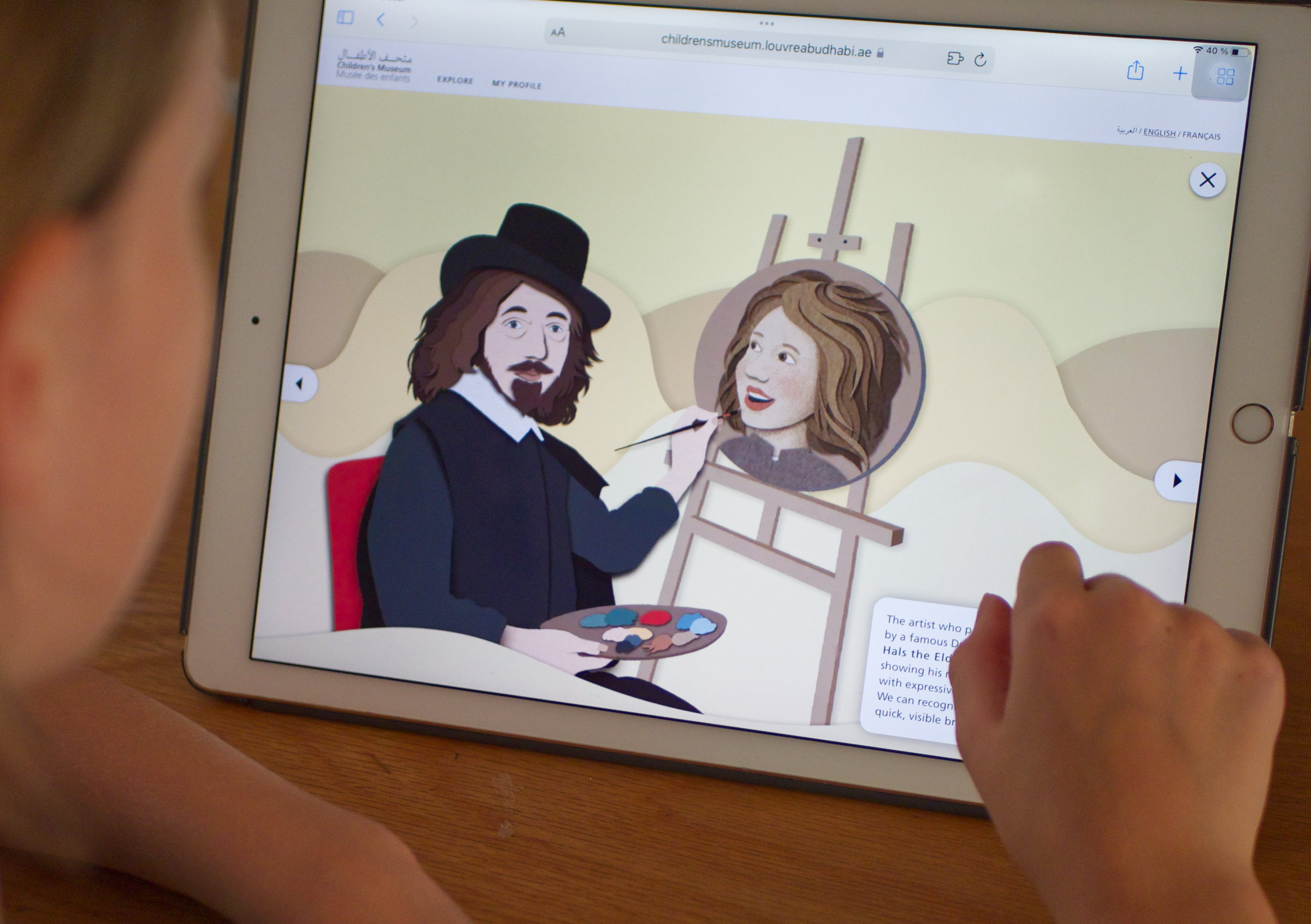 L'image montre un enfant regardant une tablette où se trouve une illustration. Sur l'écran, un artiste, habillé en costume historique avec un chapeau, peint le portrait d'une femme aux cheveux ondulés. L'artiste tient une palette de couleurs, tandis que le portrait est encadré sur un chevalet. L'arrière-plan est simple, avec des formes douces. L'enfant semble intéressé par l'image qu'il observe.
