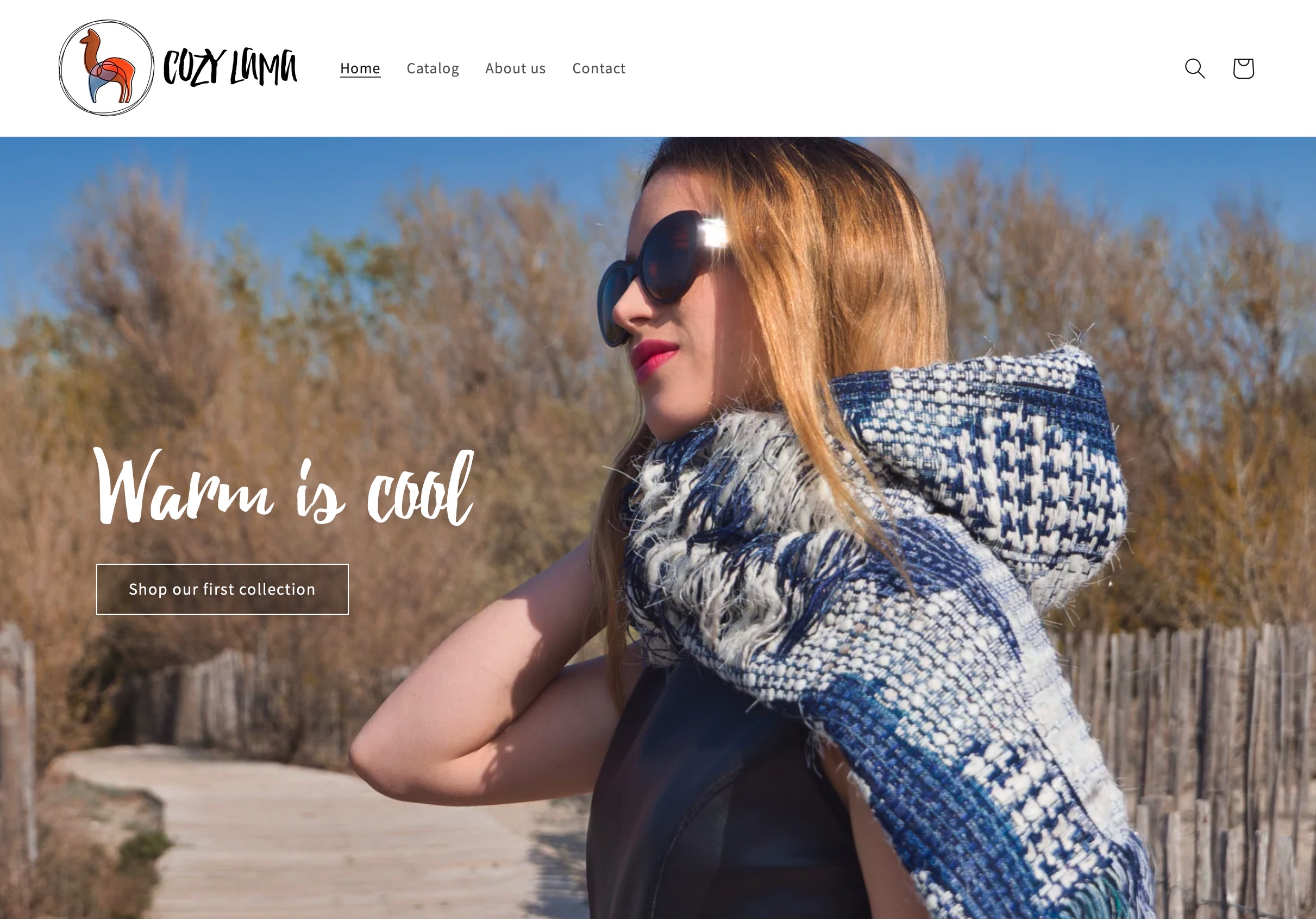 L'image présente une page d'accueil d'un site web appelé "Cozy Lummi". Au premier plan, on voit une femme portant des lunettes de soleil et une écharpe en laine. Elle semble profiter du soleil, se tenant sur un chemin entouré de nature. En arrière-plan, il y a des arbres flous. Le texte en haut de l'image indique "Warm is cool" et invite à découvrir la première collection. Le design est moderne et accueillant, avec une mise en page claire et des couleurs apaisantes.
