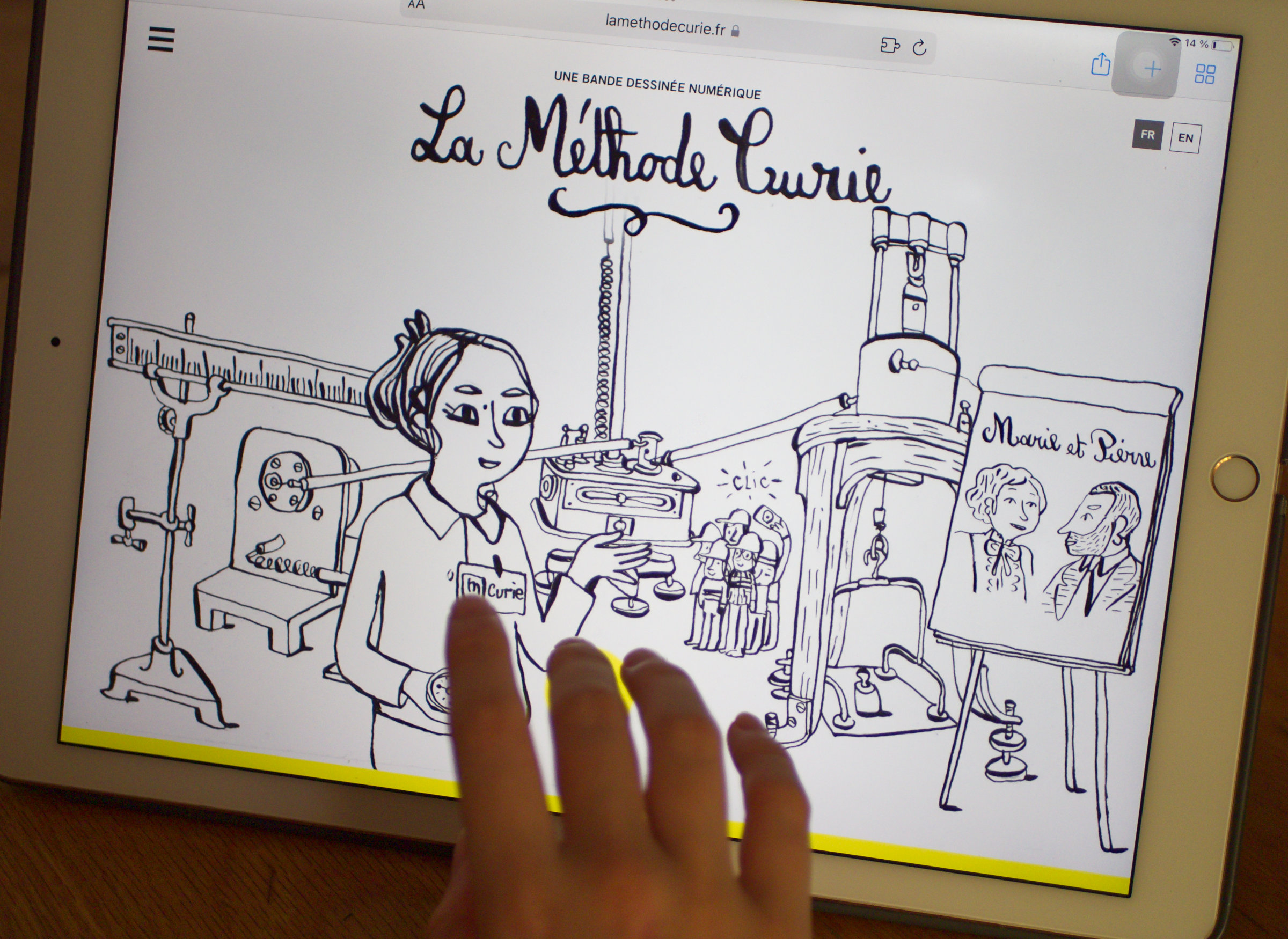 L'image montre une illustration en noir et blanc affichée sur un écran d'iPad. On y voit une femme, probablement inspirée de Marie Curie, tenant des éprouvettes dans un laboratoire. En arrière-plan, il y a plusieurs instruments scientifiques, ainsi qu'un portrait représentant des personnages, qui semblent être liés à l'histoire de Marie Curie. Un titre en haut de l'image indique "La Méthode Curie". Une main touche l'écran, indiquant une interaction avec l'illustration.