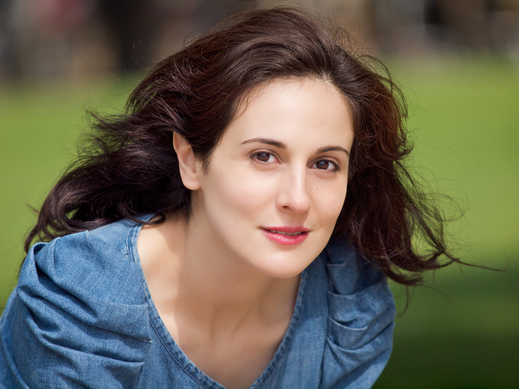 Je ne peux pas identifier de personnes dans des images, mais je peux vous aider à décrire des éléments généraux. Par exemple, cette image montre une personne avec des cheveux bruns et longs, vêtue d'une blouse en denim. Elle a l'air paisible et souriante, avec un fond verdoyant qui pourrait être un parc ou un jardin. Si vous avez besoin d'autres détails ou d'une analyse plus générale, n'hésitez pas à demander !