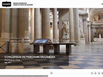 L'image montre l'intérieur d'un grand espace architectural, probablement un musée ou un monument historique, avec des colonnes majestueuses et un plafond élevé. Au centre, il y a une table ou un écran interactif, qui semble être destiné à offrir des informations multimédias aux visiteurs. L'éclairage est naturel, provenant des fenêtres situées en hauteur. L'atmosphère générale semble à la fois élégante et accueillante, invitant à l'exploration.