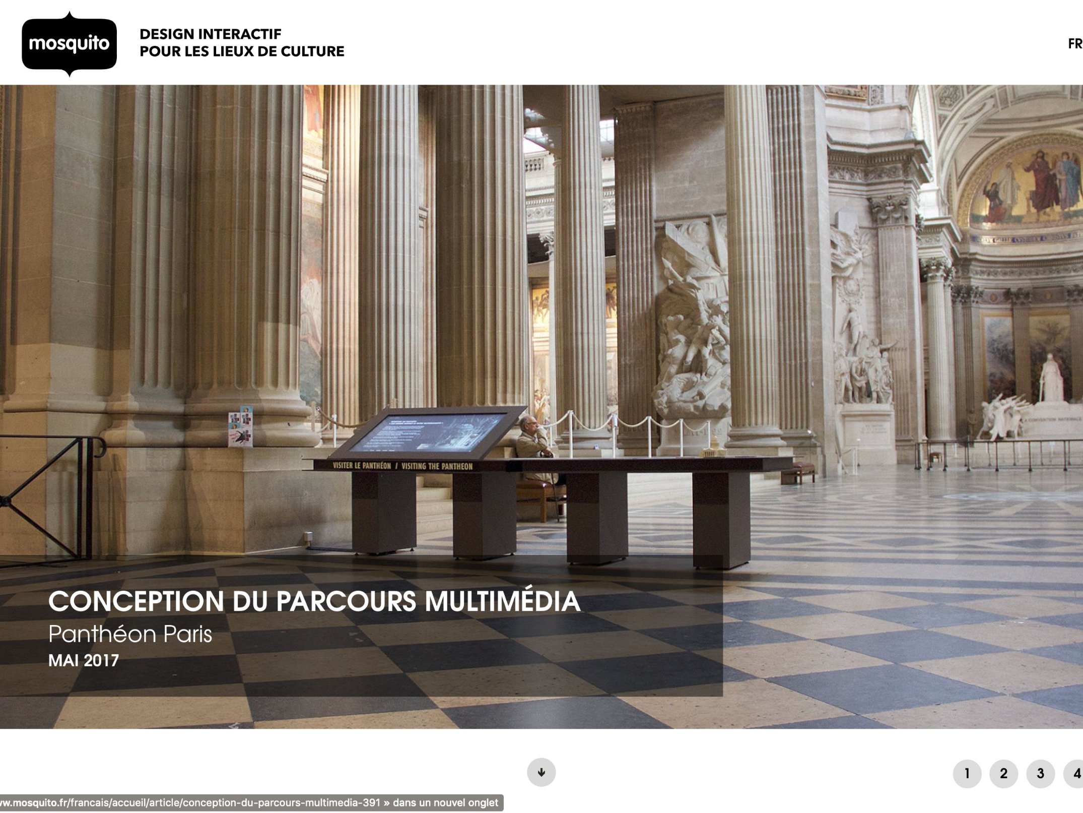 L'image montre l'intérieur d'un grand espace architectural, probablement un musée ou un monument historique, avec des colonnes majestueuses et un plafond élevé. Au centre, il y a une table ou un écran interactif, qui semble être destiné à offrir des informations multimédias aux visiteurs. L'éclairage est naturel, provenant des fenêtres situées en hauteur. L'atmosphère générale semble à la fois élégante et accueillante, invitant à l'exploration.