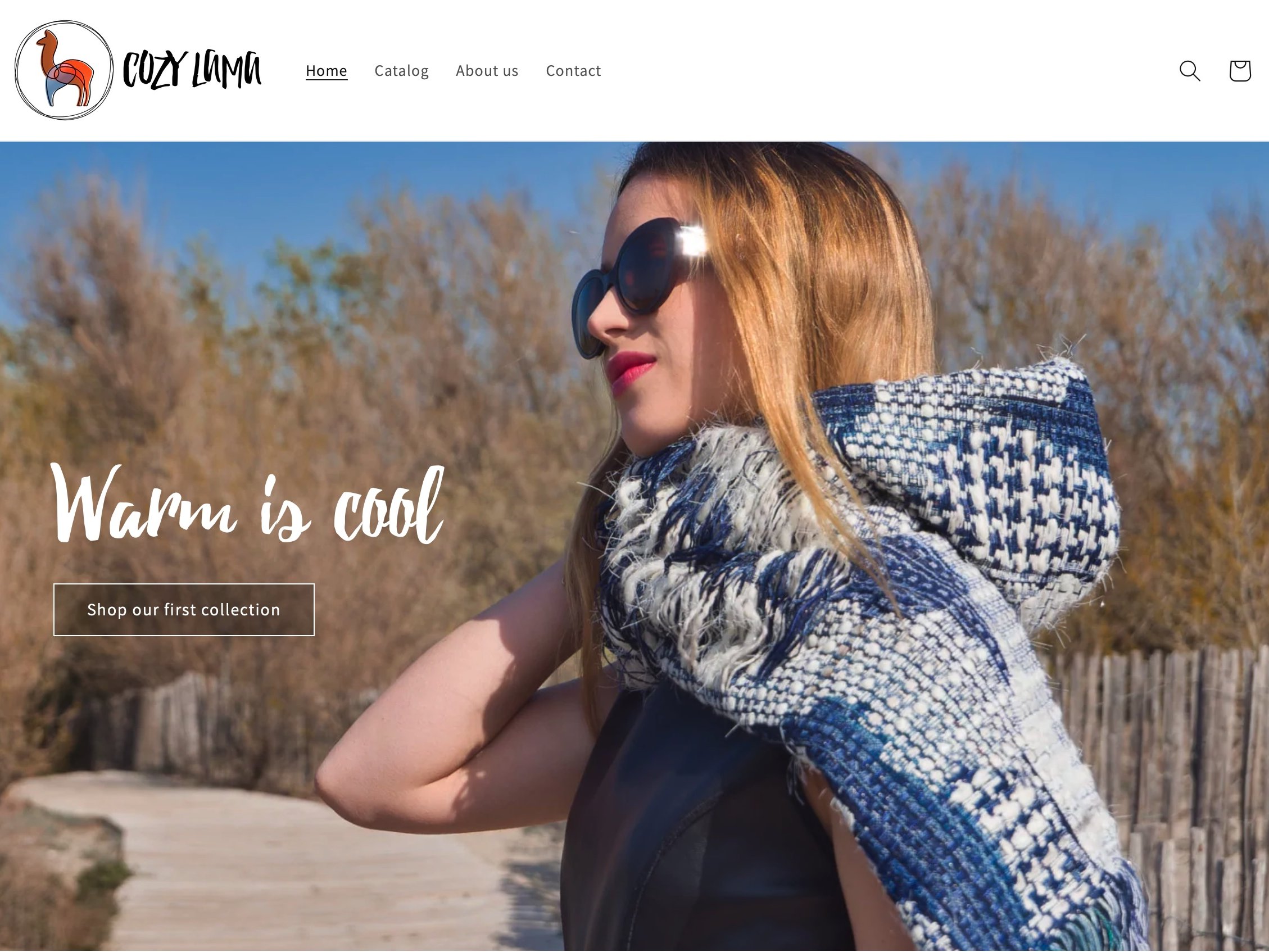 L'image présente une page d'accueil d'un site web appelé "Cozy Lummi". Au premier plan, on voit une femme portant des lunettes de soleil et une écharpe en laine. Elle semble profiter du soleil, se tenant sur un chemin entouré de nature. En arrière-plan, il y a des arbres flous. Le texte en haut de l'image indique "Warm is cool" et invite à découvrir la première collection. Le design est moderne et accueillant, avec une mise en page claire et des couleurs apaisantes.
