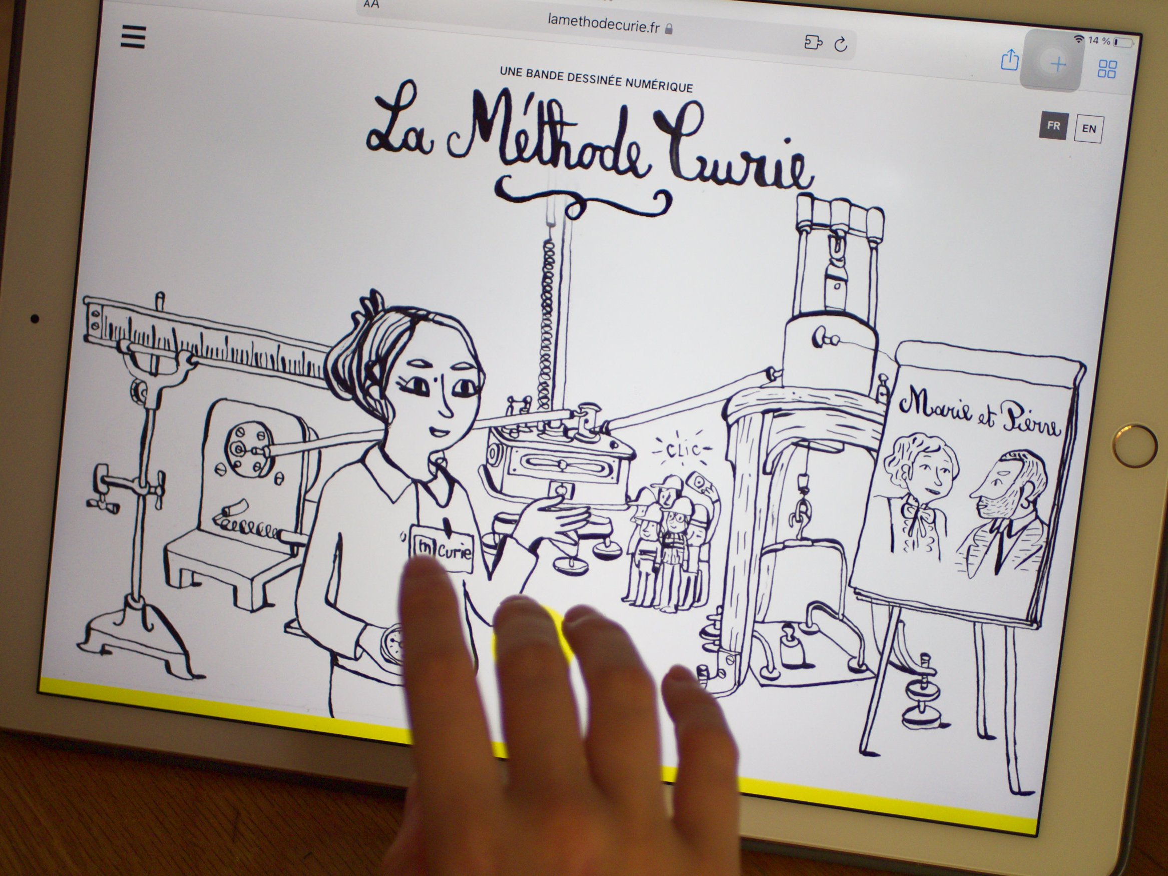 L'image montre une illustration en noir et blanc affichée sur un écran d'iPad. On y voit une femme, probablement inspirée de Marie Curie, tenant des éprouvettes dans un laboratoire. En arrière-plan, il y a plusieurs instruments scientifiques, ainsi qu'un portrait représentant des personnages, qui semblent être liés à l'histoire de Marie Curie. Un titre en haut de l'image indique "La Méthode Curie". Une main touche l'écran, indiquant une interaction avec l'illustration.