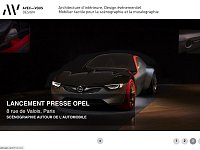 L'image montre une automobile moderne et futuriste mise en valeur dans un cadre sombre et élégant. La voiture, aux lignes aérodynamiques, est présentée sur un podium, entourée d'une ambiance de lumière tamisée qui accentue ses formes. Le fond est minimaliste, ce qui permet de concentrer l'attention sur le véhicule. En bas, on peut voir des informations sur l'événement de lancement de l'Opel, situé à Paris.