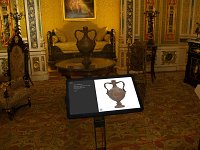 L'image montre une pièce richement décorée, probablement dans un musée ou un palais, avec des détails architecturaux élaborés. Au centre, il y a une table sur laquelle repose une tablette affichant une représentation d'une belle urne ou vase ornée. En arrière-plan, on aperçoit un canapé et des chaises élégantes, toutes avec des motifs raffinés. Le sol est recouvert d'un tapis orné aux couleurs vives. Les murs sont décorés avec des motifs complexes et des œuvres d'art. L'ensemble dégage une atmosphère historique et artistique.
