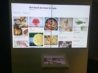 L'image montre un affichage numérique composé de plusieurs écrans côte à côte, présentant un collage de diverses images de plats alimentaires. Il y a des titres en anglais, notamment "the food we love to hate", suggérant un thème lié à la nourriture qui suscite des avis partagés. En bas, un écran ou une tablette affiche probablement des images supplémentaires ou des détails sur les plats présentés. L'ensemble donne une impression moderne et interactive, invitant à explorer les différents mets.